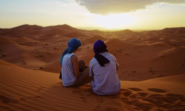 two men sitting on sand dunes