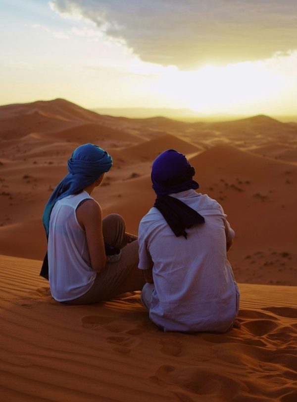 two men sitting on sand dunes