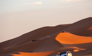 A car driving through the desert with sand dunes in the background